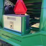 A silver control box marked ACJ Maskiner, with a red warning triangle above it on a GreenLoader.
