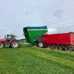 A red tractor and GreenLoader beside a red trailer on a grass field.