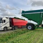 A raised GreenLoader unloading into a red trailer behind a white truck.