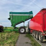 A raised GreenLoader tilted over a red trailer, with people standing nearby.