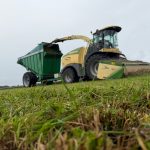 A forage harvester and GreenLoader seen across long grass.