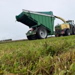 A raised GreenLoader and a forage harvester stopped on grass.