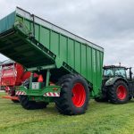 Rear three-quarter view of a raised GreenLoader hitched to a tractor with red wheels.