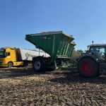 A tractor and raised GreenLoader beside a yellow truck in maize stubble.