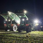 A GreenLoader with its body raised, working under work lights at night.