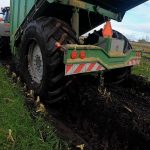 Low rear view of a GreenLoader moving through muddy maize rows.
