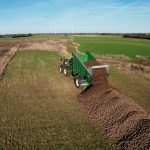 Aerial view of a GreenLoader leaving a long pile of root crop across a field.