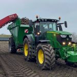 A tractor and GreenLoader alongside a red root-crop harvester.