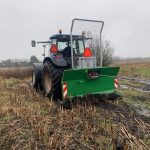 Rear view of a tractor with a green PowerWinch blade on stubbly ground.