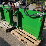 Two green PowerWinch mounting frames with hydraulic hoses, standing on a pallet.