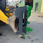 Close-up of the green hitch brackets where a PowerWinch meets a loader arm.
