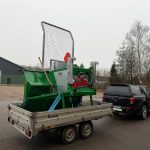 A green PowerWinch strapped on a flatbed trailer behind a dark pickup.