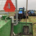 View over a PowerWinch blade toward two blue tractors in a field.